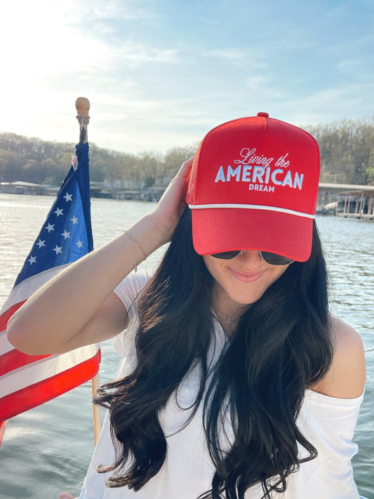 Woman wearing a red cap with 'Living the American Dream' text on a boat with an American flag.